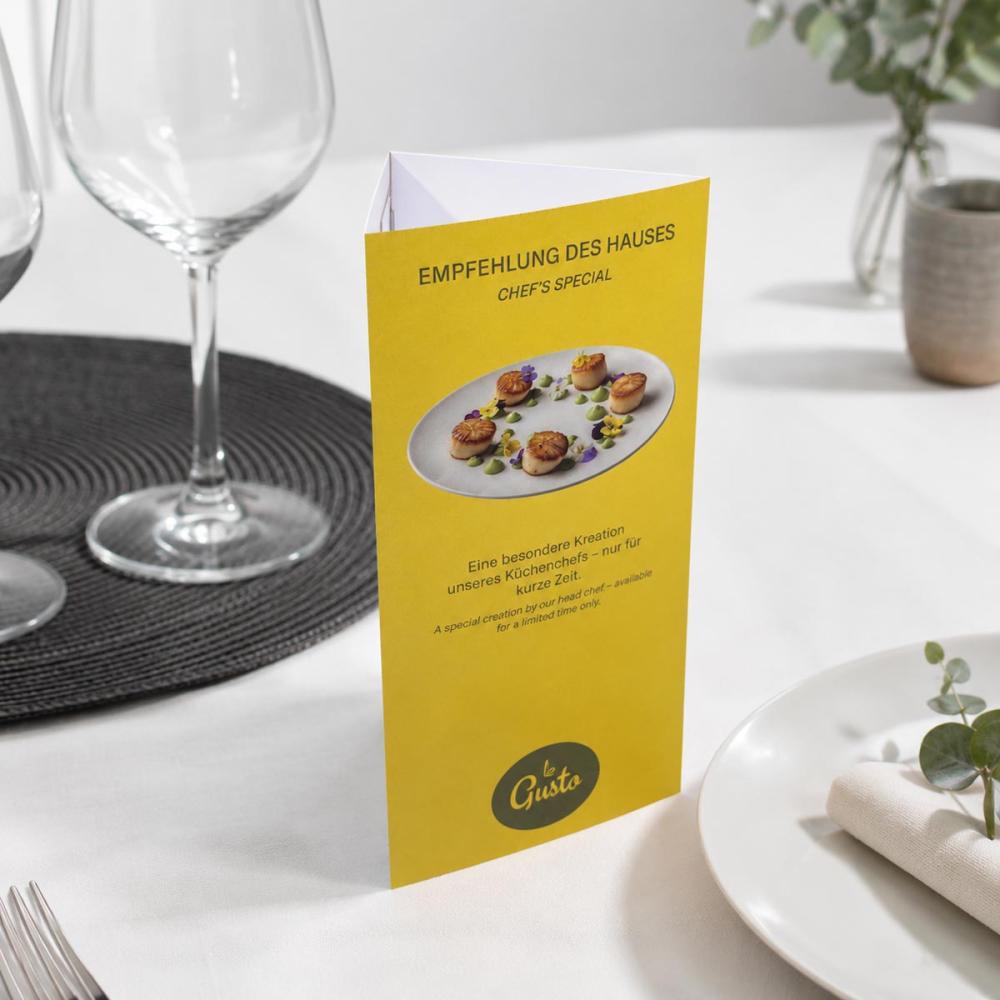 Chevalet de table prisme imprimé, au design jaune présentant une suggestion du chef, sur une table dressée au restaurant.